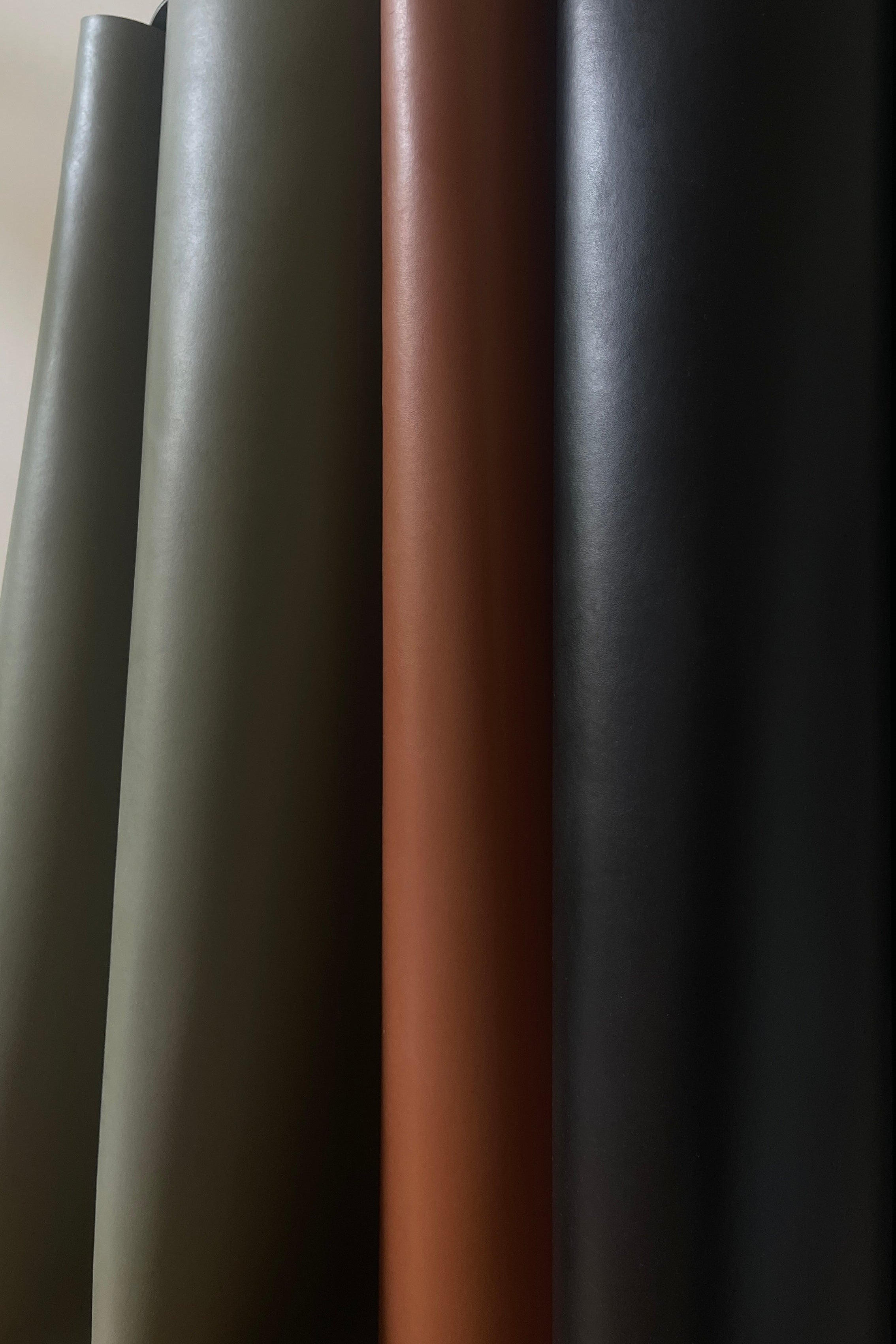 Three rolls of black, cognac and olive leatherette with different textures on a neutral background