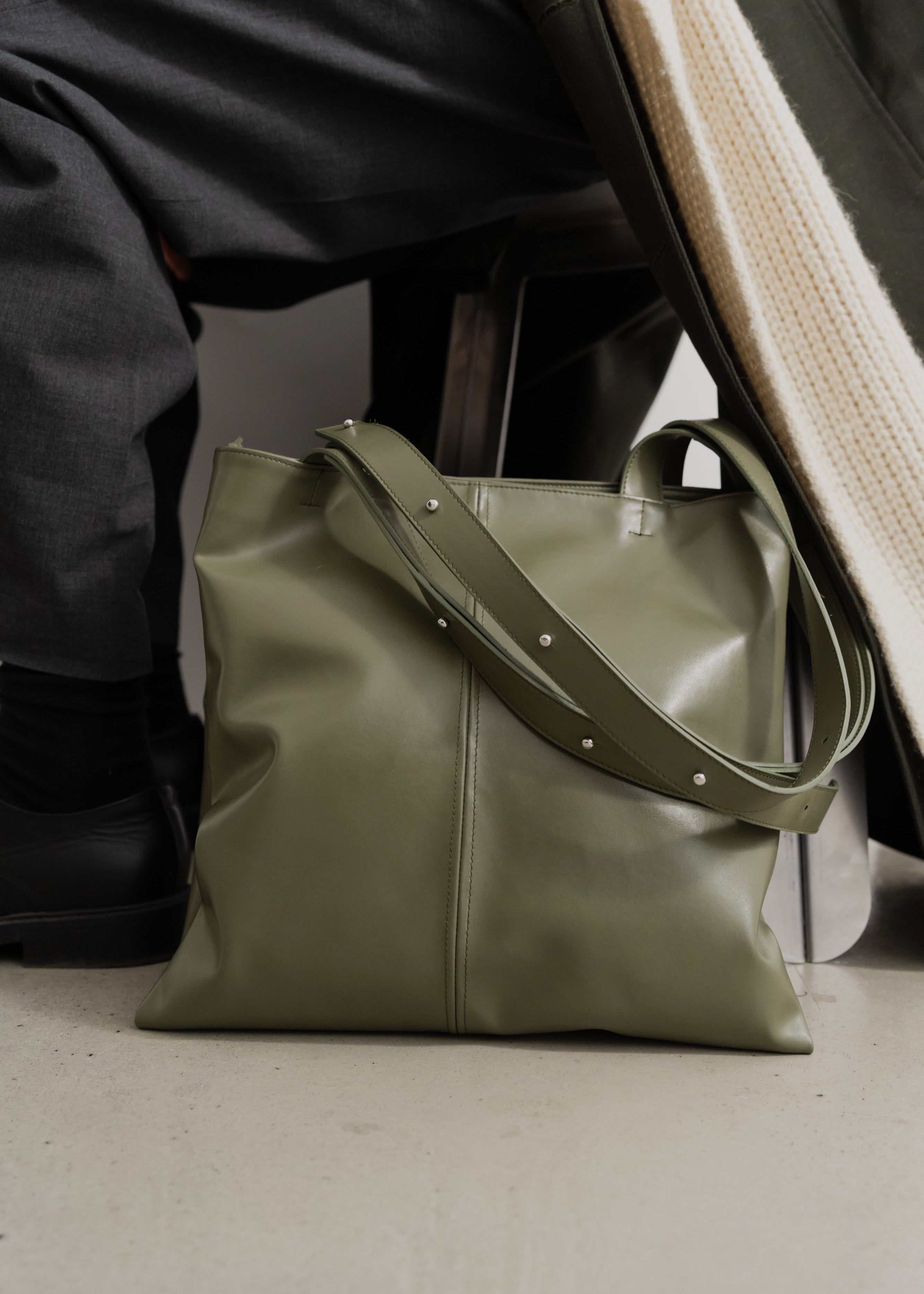 Green leather handbag on a light gray surface with a blurred background